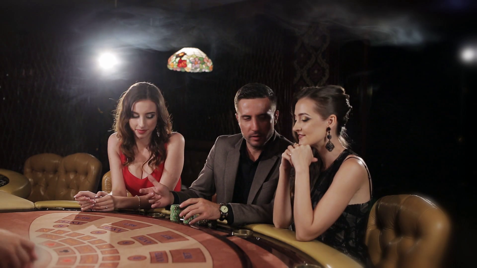 Богатій мужчина играет в покер в компании двух привлекательных девушек