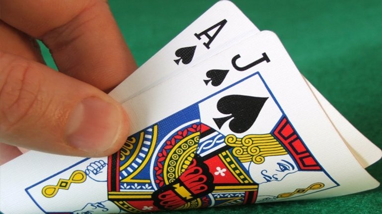 Рука игрока переворачивает две карты - пиковый туз и пиковый валет