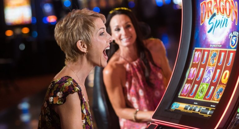 Женщинга с короткой стрижкой в вечернем платье отрывается в казино за игрой на автоматах
