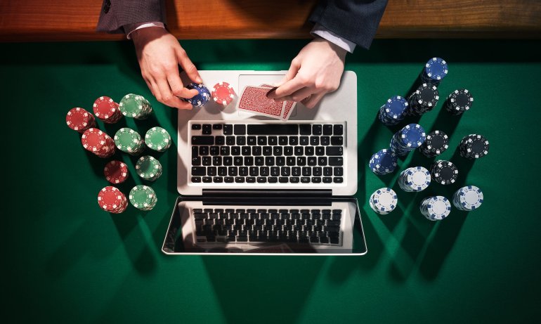 Игрок сидит у ноутбука, а рядом стопки фишек для казино