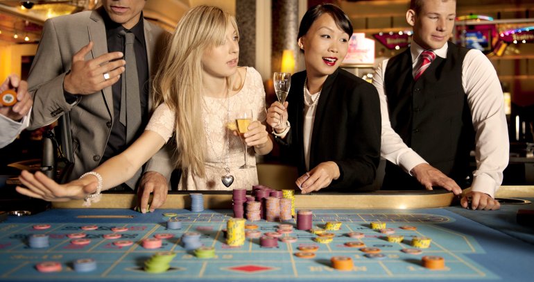 Симпатичная блондинка и ее подруга китаянка распивают шампанское играя в рулетку в компании обеспеченных мужчин