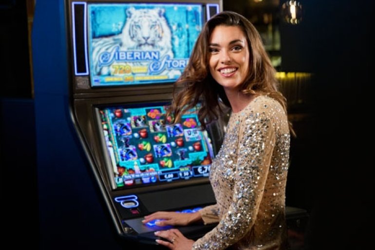 Симпатичная девушка в блестящем платье сидит перед игровым автоматом с довольной улыбкой на лице