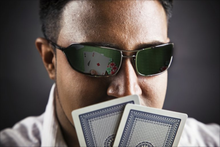 Мужчина держит перед собой две карты, а в его очках отражаются два туза пиковой и бубновой масти