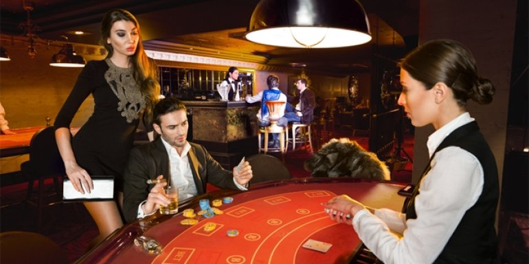 Серьезный мужчина в костюме и с сигарой в руках играет в казино, а его спутница, сексуальная модель, стоит рядом