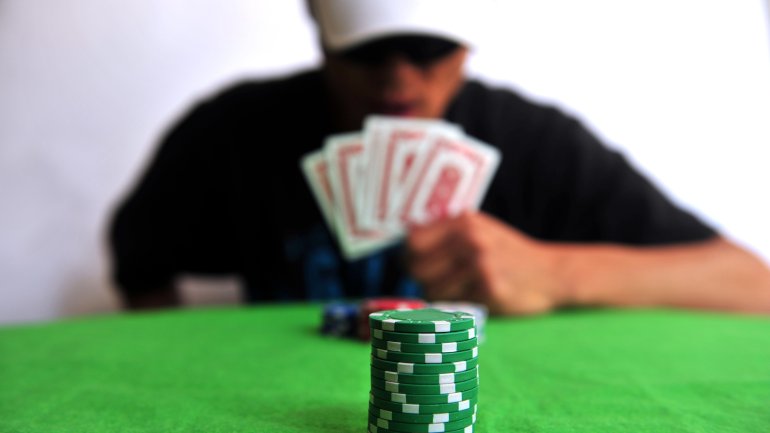 Стопка фишек на покерном столе, а напротив игрок, прикрывающий лицо картами