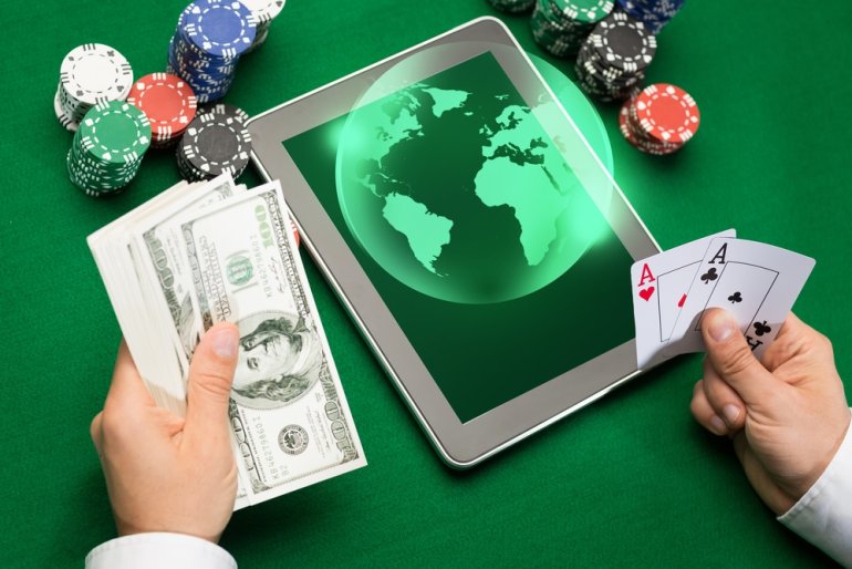 На игорном столе зеленого цвета планшет, карты, фишки и руки игрока, который собирается совершить ставку